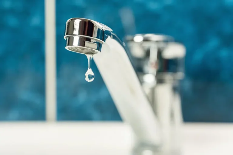 Close-up view of a leaking faucet with a visible water droplet forming at the aerator.