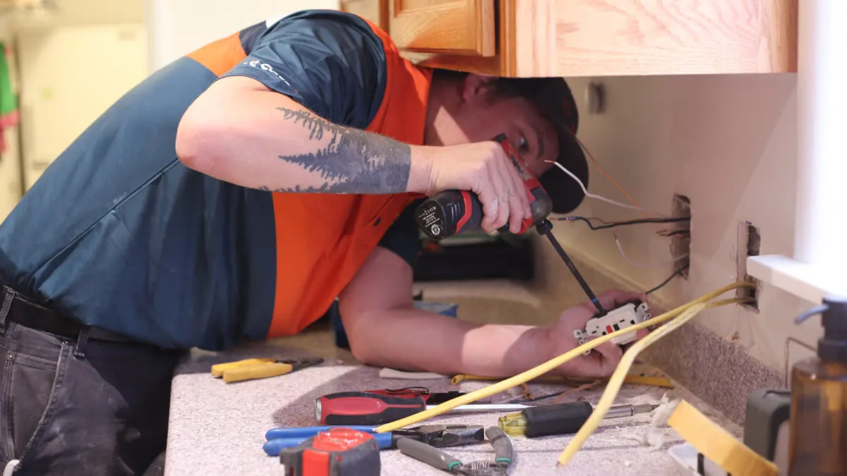 Harts electrician installing a new wall outlet with tools spread on the countertop