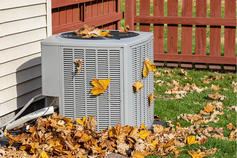 HVAC unit outside a home with autumn leaves gathered around it