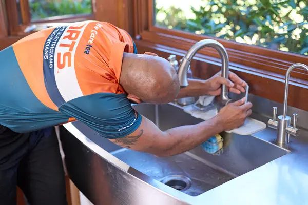 Plumber installing a kitchen sink faucet and plumbing fixtures.