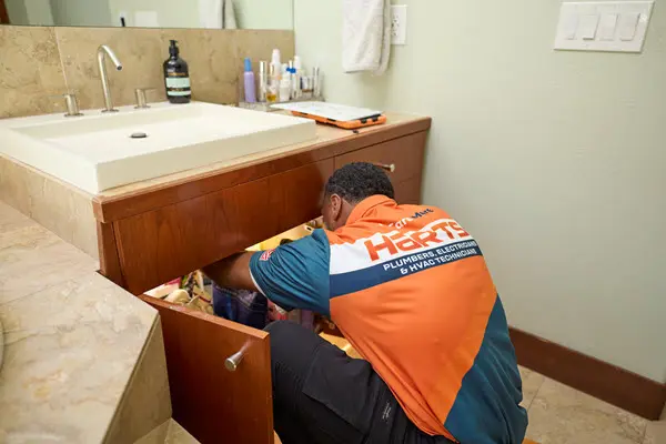 Plumber inspecting plumbing connections under a bathroom sink before a leak repair.