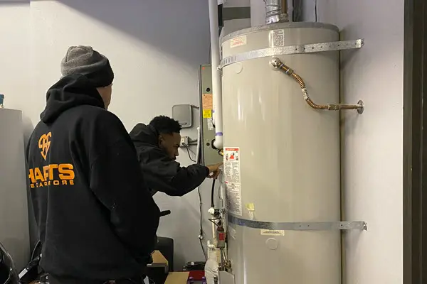 Plumbers servicing a residential water heater system in a utility room.