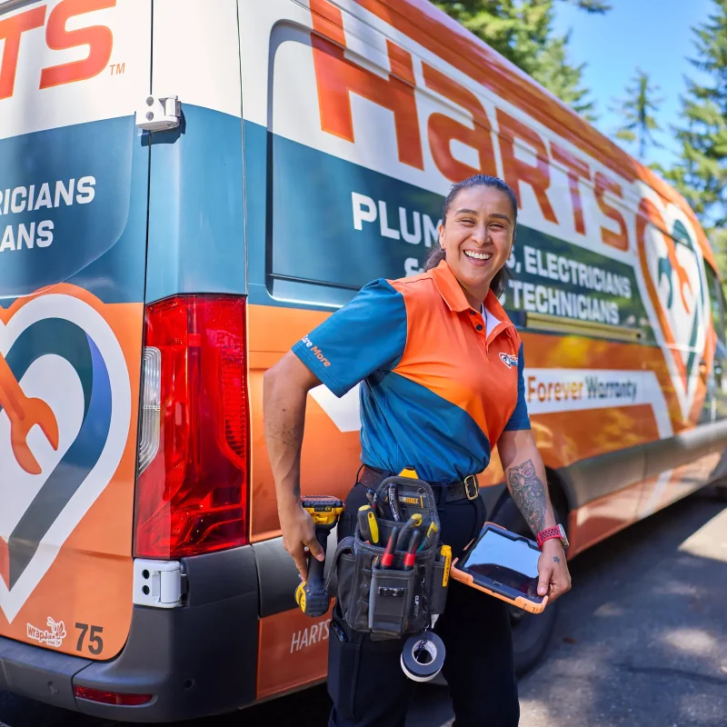 harts-technician-with-service-van Harts technician in branded uniform smiling beside a fully wrapped Harts service van.